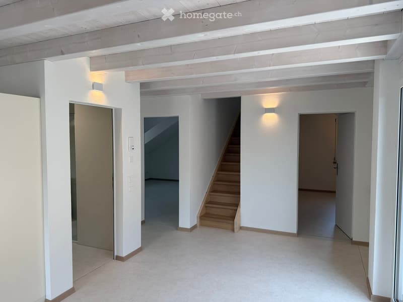Empty hallway with white walls, wooden staircase, and recessed lighting. No furniture or equipment present.
