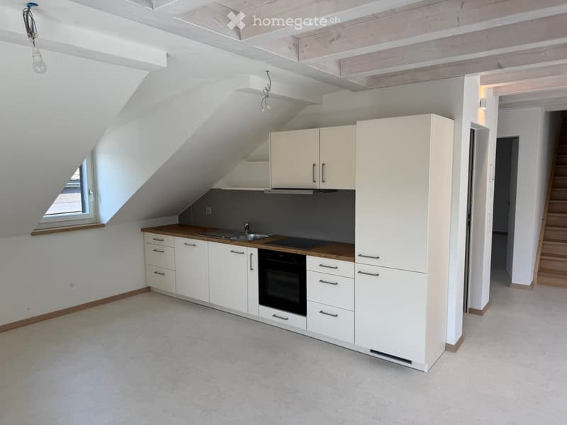 Modern kitchen with white cabinets, wooden countertops, stainless steel sink, and built-in oven. The space features exposed wooden beams and a skylight window.