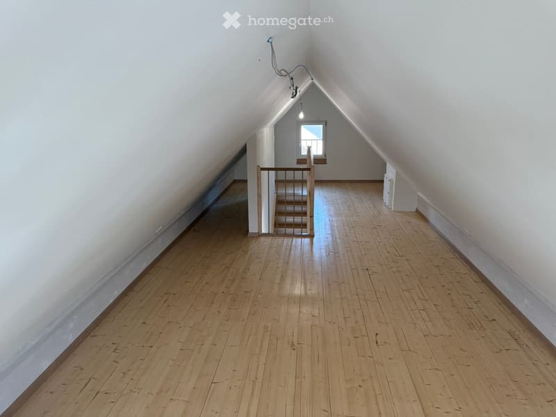 Empty attic space with wooden flooring, white walls, and a small window at the far end. A staircase leads up to the attic from the left side.