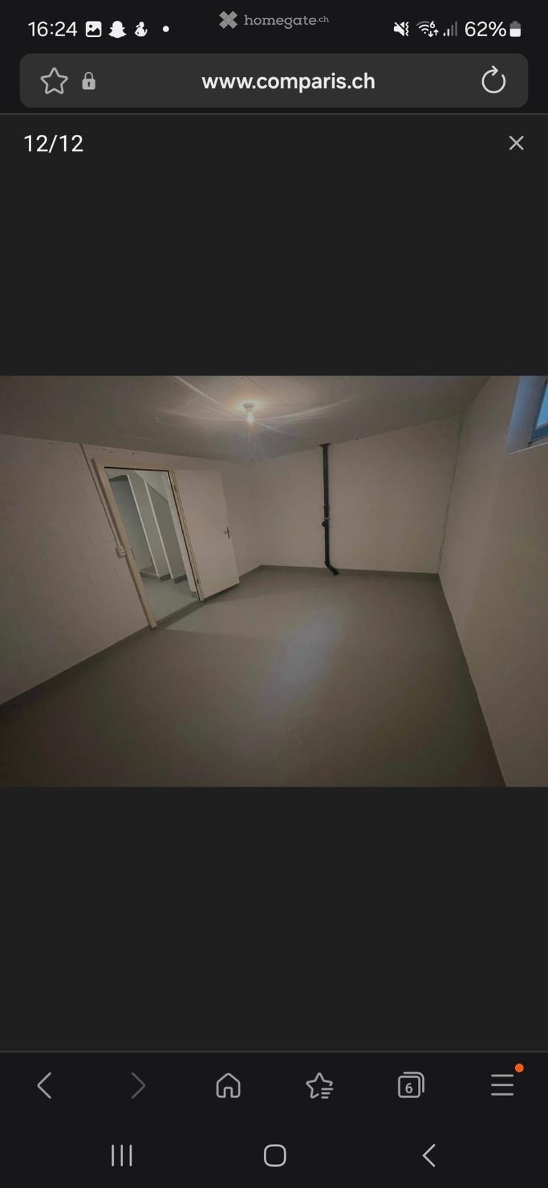 Empty room with bare walls and a concrete floor, featuring a single light fixture on the ceiling and a partially open door leading to another space.