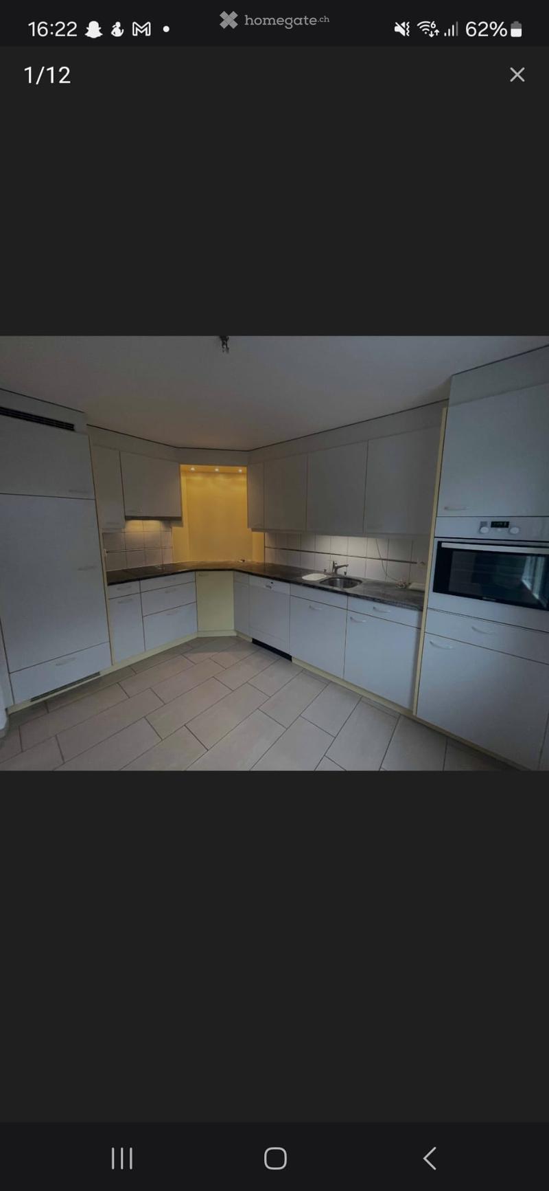 Modern kitchen with white cabinets, a sink, and an oven, featuring tiled flooring and warm lighting.