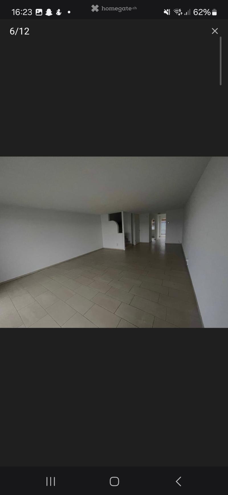 Empty hallway with tiled floor and white walls, leading to an open doorway at the end.