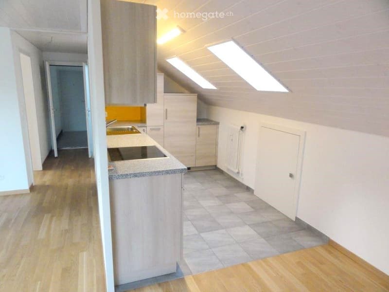 Modern kitchen with light wood cabinets, granite countertop, stainless steel sink, and stove. Skylight windows provide natural light. Wooden flooring throughout.