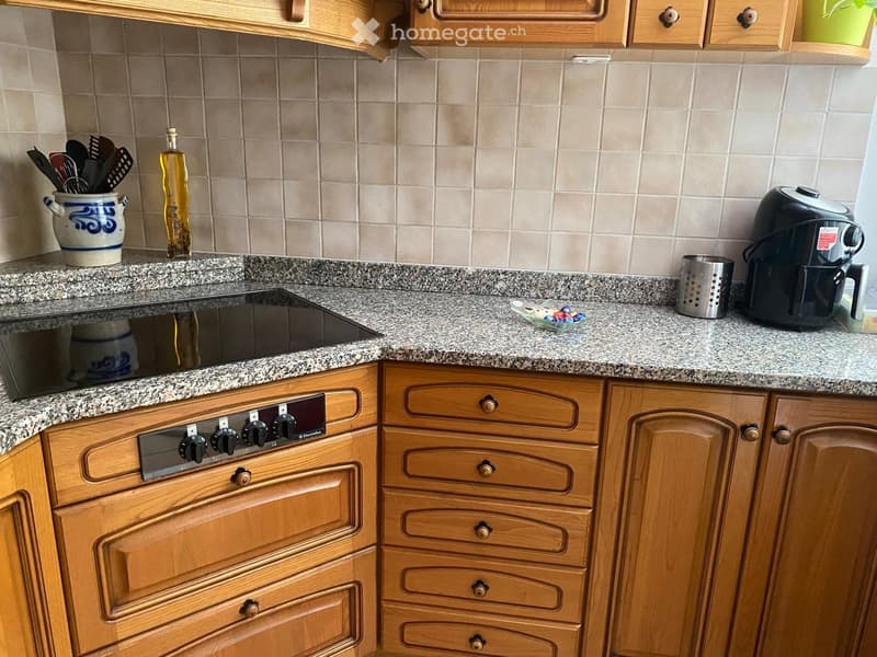 kitchen with granite countertop, wooden cabinets, black induction stove, black air fryer, stainless steel strainer, oil bottle, and a blue and white ceramic jar