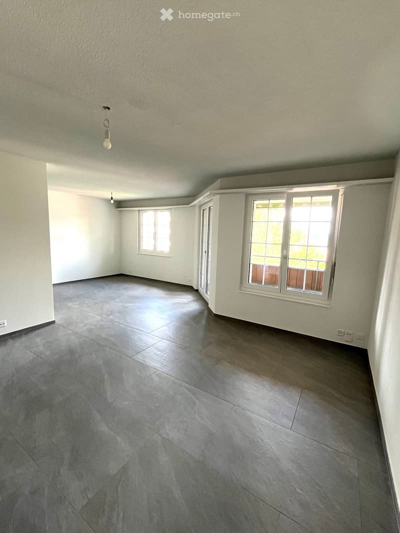 Empty room with grey tiled floor, white walls, and two windows, one with a sliding door.