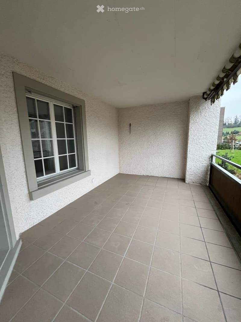 Empty balcony with tiled floor, white walls, and a window opening to the left.