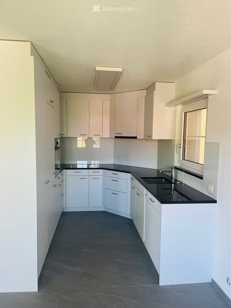 Modern, unfurnished kitchen with white cabinets, black countertops, and a sink. The space features a dark tiled floor and large windows allowing natural light.