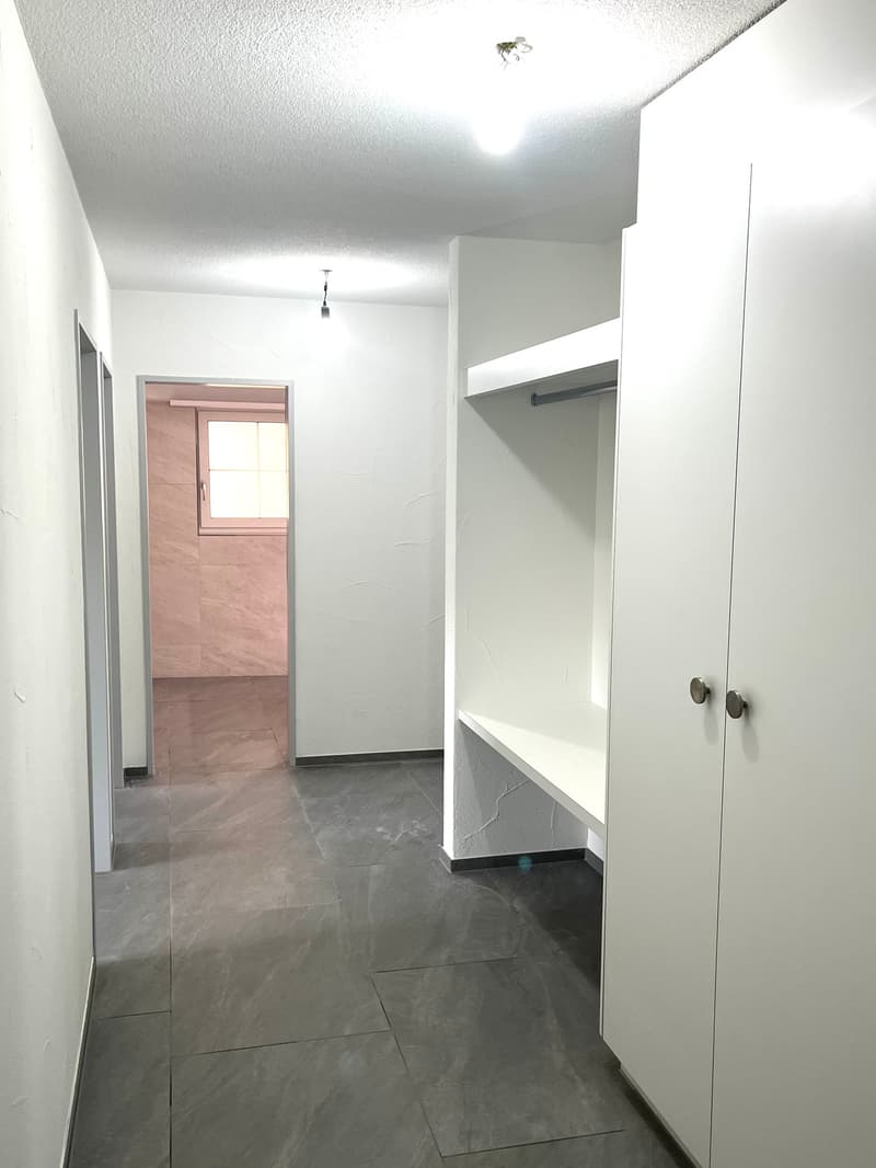 Empty hallway with white walls, gray tiled floor, built-in closet with shelves, and a small window at the end.
