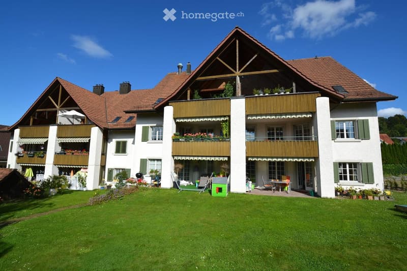 Two-story house with white walls, green shutters, red-tiled roof, multiple balconies, and a well-maintained lawn.