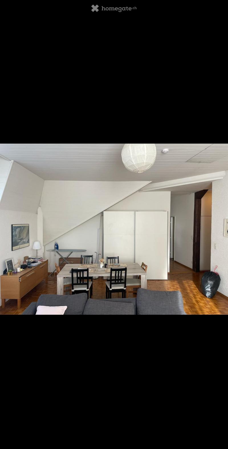 Bright living and dining area with wooden flooring, white walls, and modern furniture including a sofa, dining table, chairs, and a cabinet.