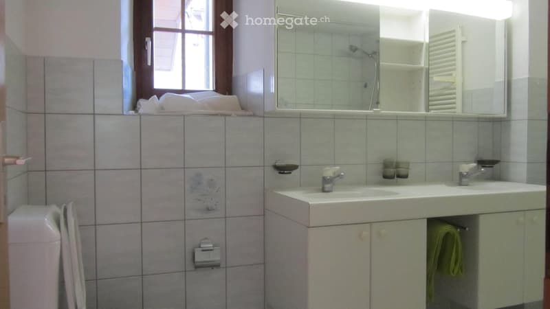 Bathroom. Bathroom with tiled walls, a double sink, a large mirror, a cabinet, and a towel hanging on the cabinet door.
