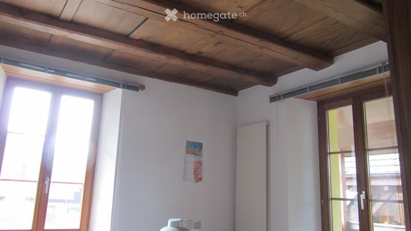 Unfurnished Room. Empty room with wooden ceiling, large windows, and a radiator. No furniture or equipment present.