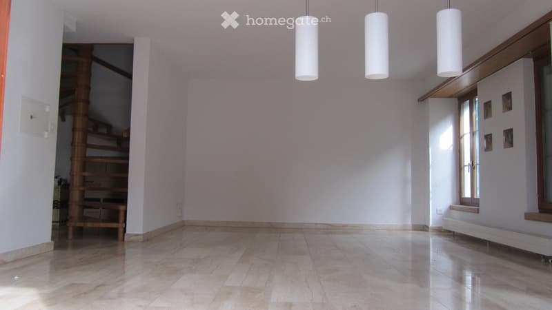 Corridor / Hallway. Empty hallway with tiled floor, white walls, and a spiral staircase leading upwards. Three pendant lights hang from the ceiling, and there is a window on the right side.