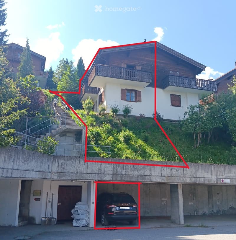 Two-story house with white walls, wooden balconies, and a raised ground floor leading to a garage with a parked car.