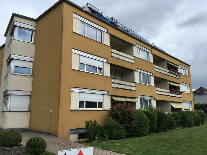 Four-story residential building with beige and yellow facade, multiple windows, balconies, and rooftop signage.