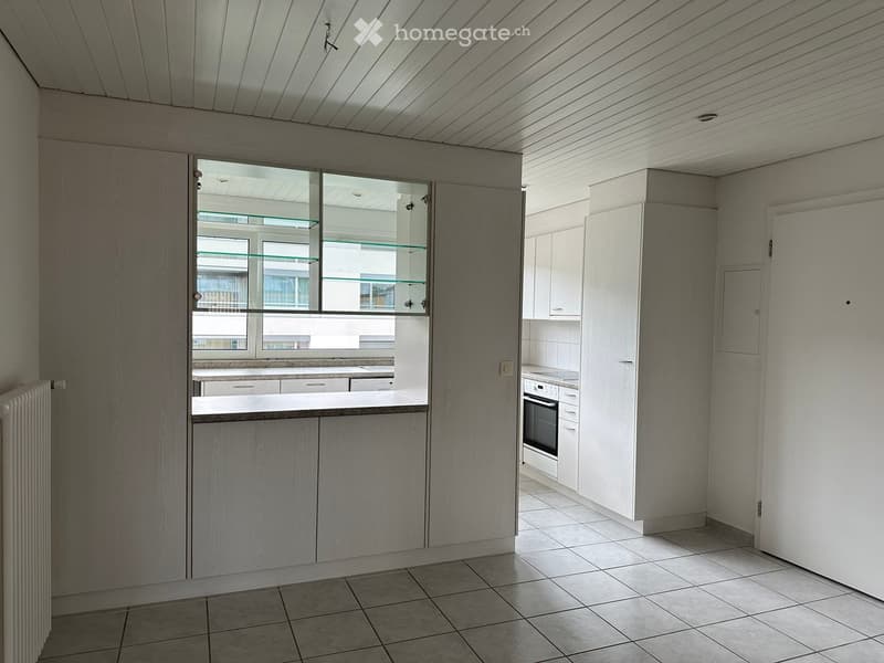 Modern kitchen with light grey cabinets, tiled floor, and a built-in oven. Features a large window with glass shelves and a radiator on the left side.