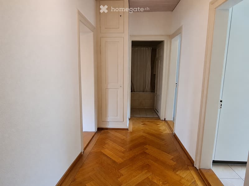A narrow hallway with wooden herringbone flooring, white walls, and several doors leading to different rooms.