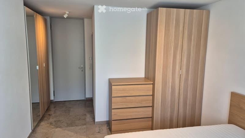 Bedroom with wooden bed, wooden wardrobe, wooden chest of drawers, white walls, tiled floor, mirror, door