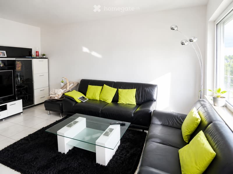 Modern living room with black leather sofas, bright yellow cushions, a glass coffee table, a black shag rug, and a sleek TV stand.