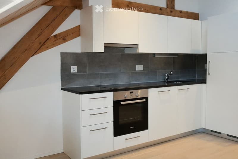 Modern kitchen with white cabinets, black countertops, stainless steel oven, and a sink with a faucet.