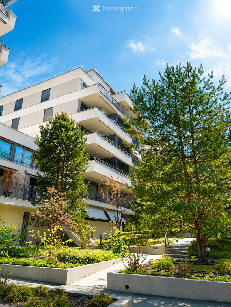 Building. Modern multi-story residential building with balconies, surrounded by greenery and trees.