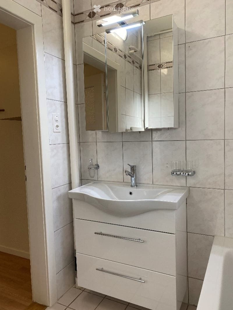 Modern bathroom with a white sink, mirrored cabinet, and tiled walls.