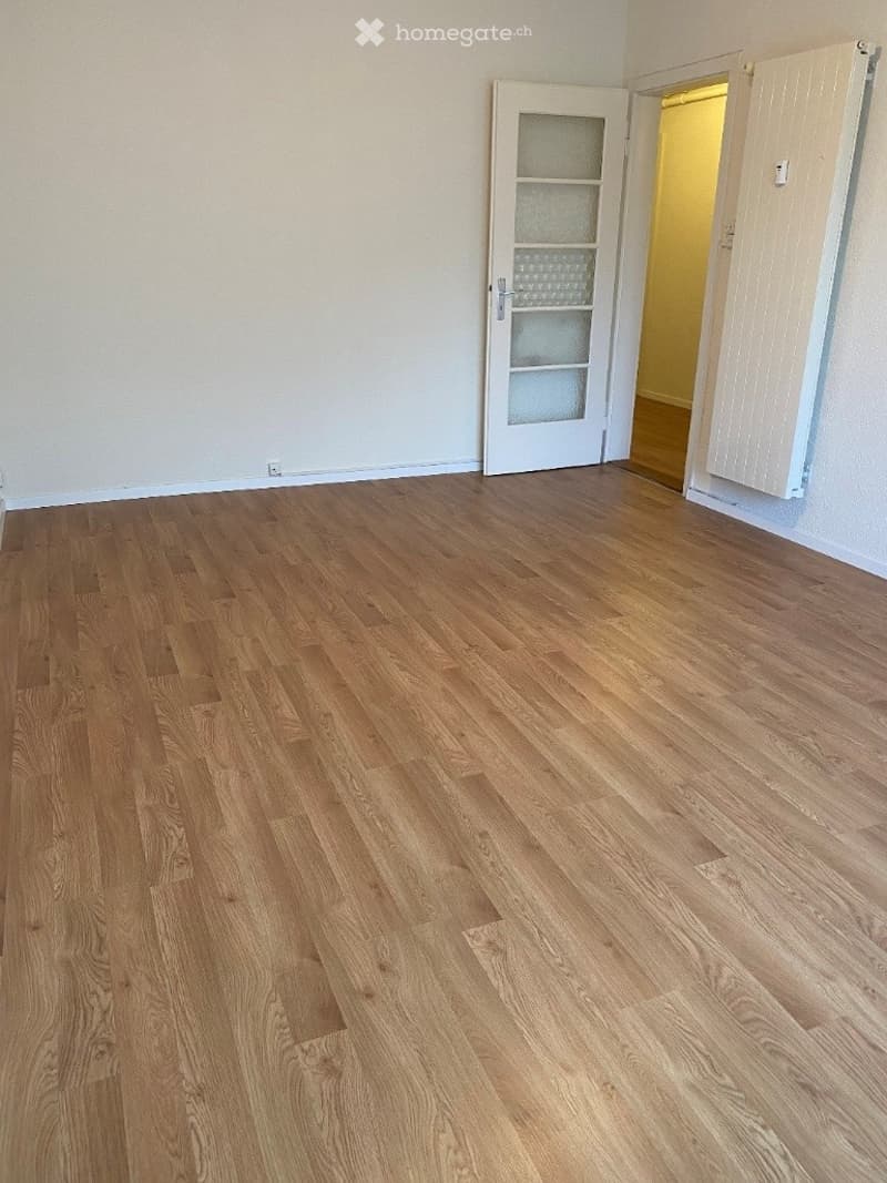 Empty room with wooden flooring, white walls, and a white door with glass panels leading to another room.