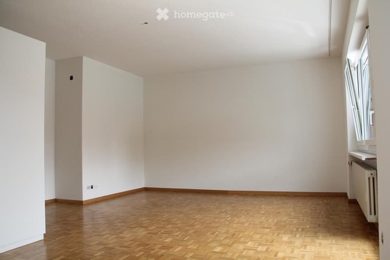 Empty room with wooden flooring and white walls, featuring a window with blinds and a radiator on the right side.