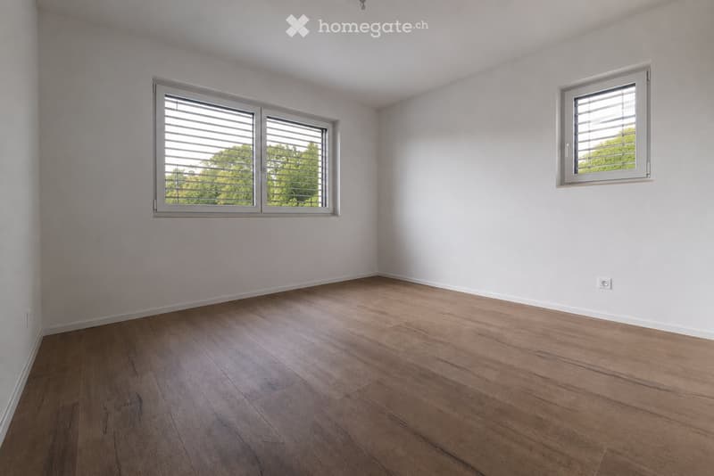 Empty room with light-colored walls, wooden flooring, and two windows with blinds. No furniture or equipment is present.