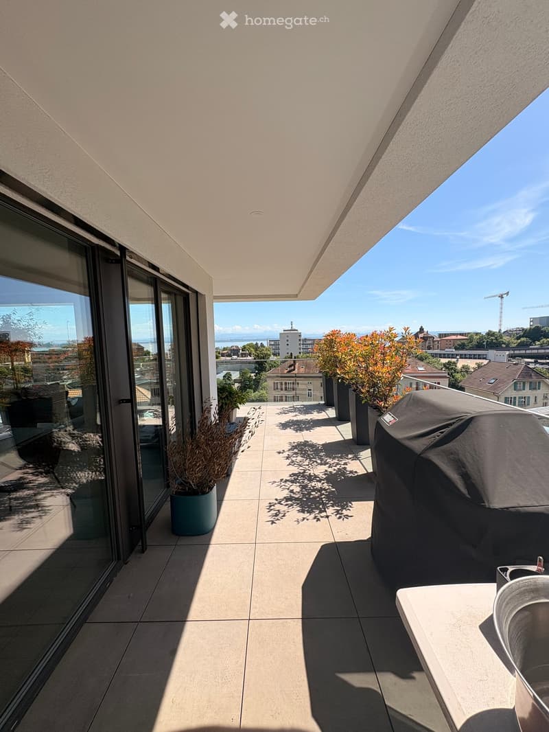 Modern balcony with tiled floor, large glass sliding doors, potted plants, and a covered grill. Offers a scenic city view.