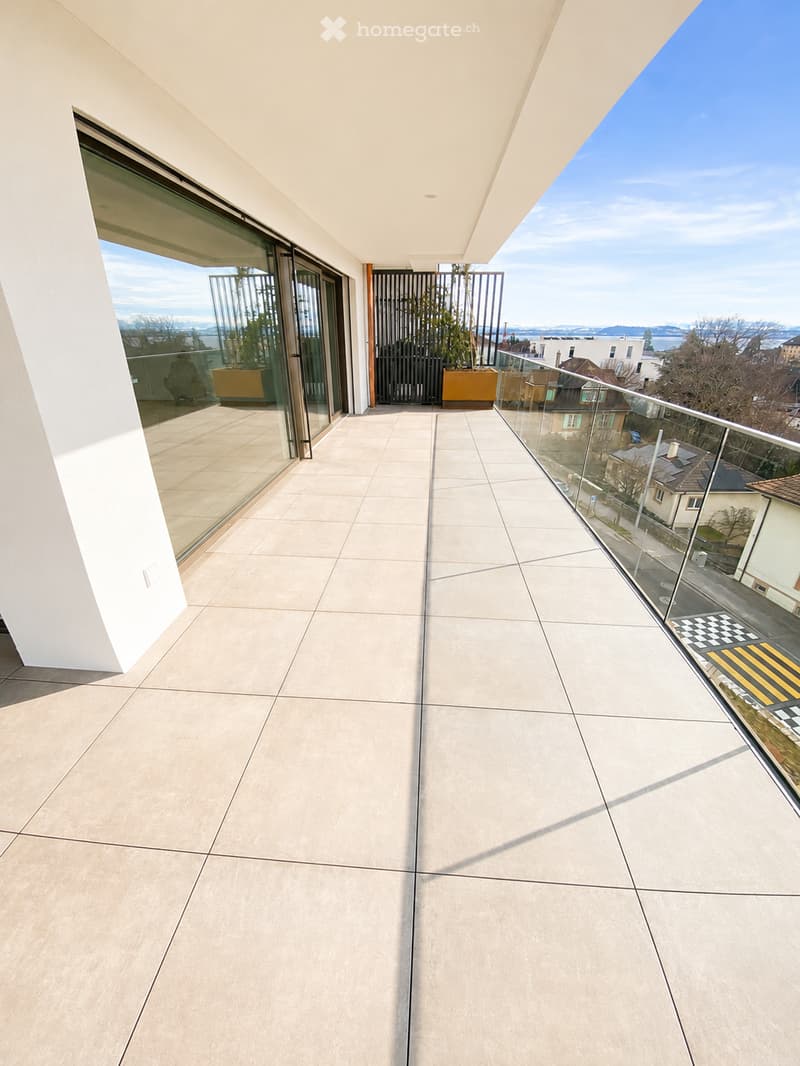 Modern balcony with large glass railings, tiled floor, and scenic city view.