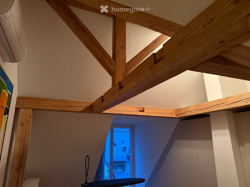 A hallway with exposed wooden beams and a skylight, leading to a blue-lit room beyond.