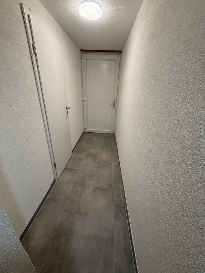 Empty hallway with tiled floor, white walls, and a closed door at the end.
