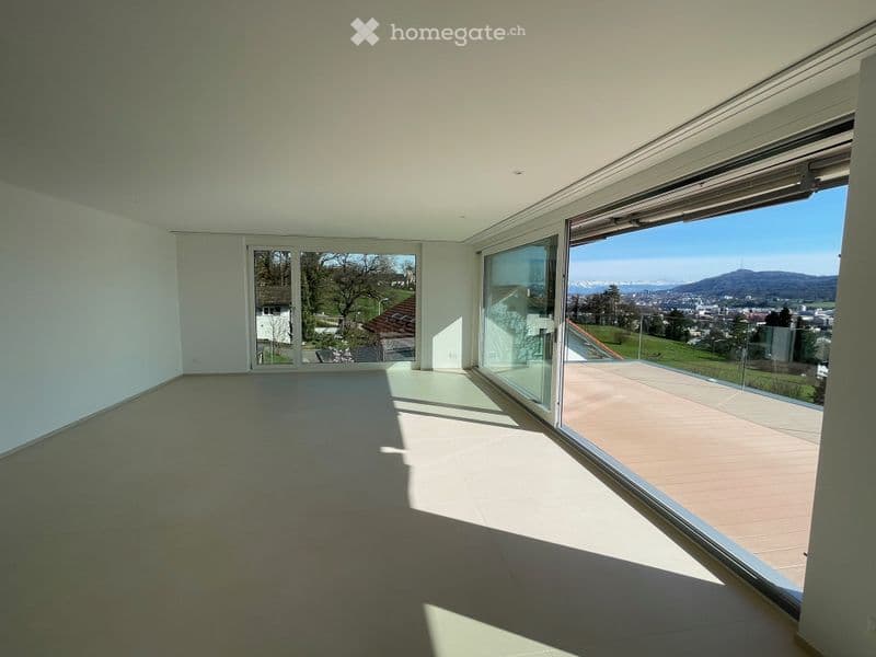 Empty room with large glass sliding doors leading to a balcony, offering a scenic view of the landscape and city.