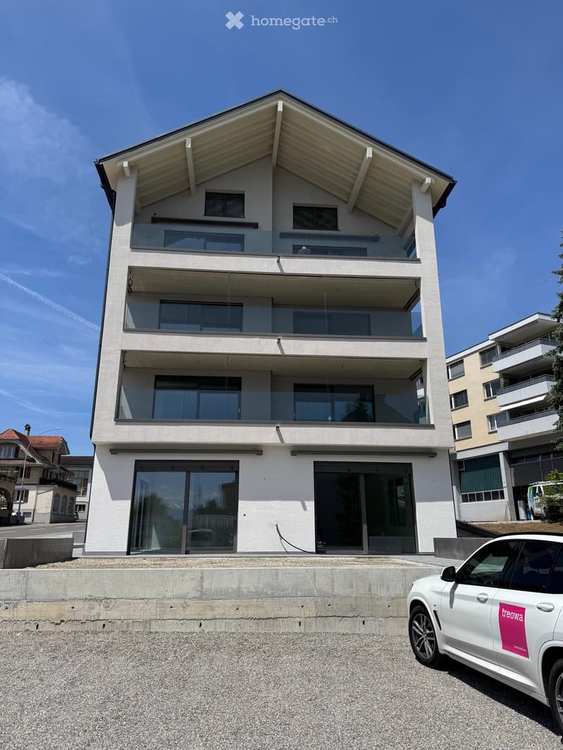 Modern three-story house with large glass balconies and a raised ground floor, featuring a sleek design and contemporary architecture.