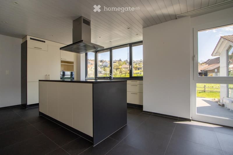 Modern kitchen with a central island, white cabinets, dark countertops, and large windows offering a view of the surrounding area.