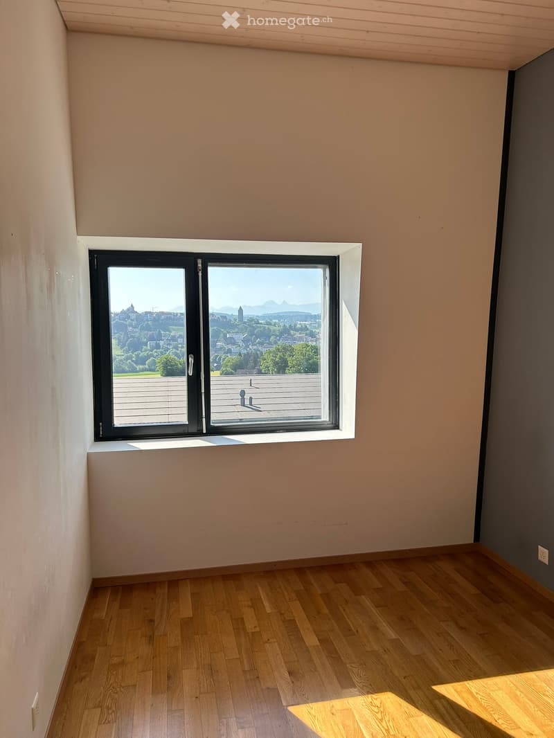 Empty room with wooden flooring, light-colored walls, and a large window offering a scenic view of a city and landscape.