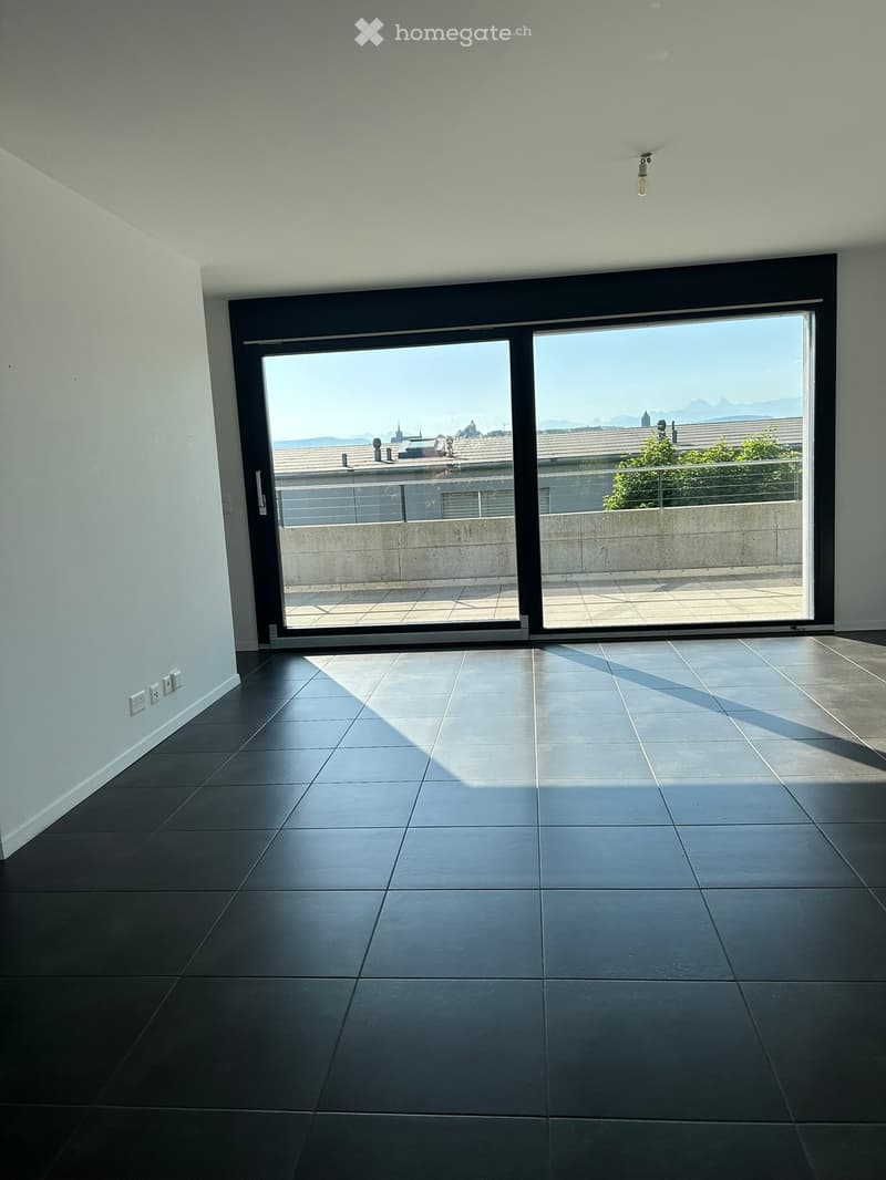 Empty room with dark tiled flooring, white walls, and large sliding glass doors leading to a balcony with a city view.
