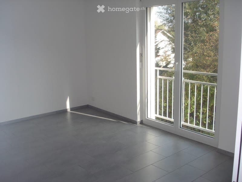 Empty room with grey tiled floor, white walls, and large sliding glass doors leading to a balcony.