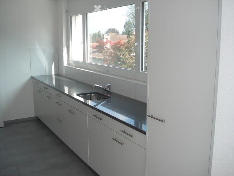 Modern kitchen with white cabinets, stainless steel sink, and large window overlooking a garden.