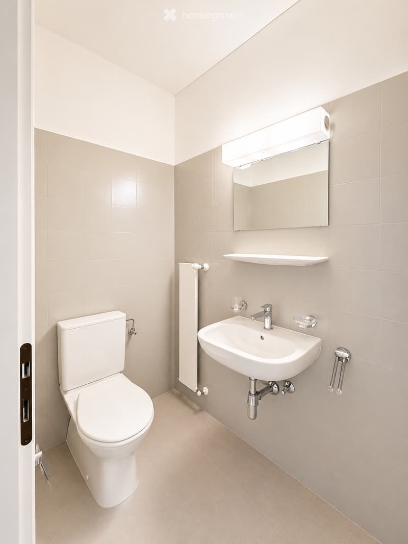Modern bathroom with beige tiles, white toilet, sink, mirror, and radiator.