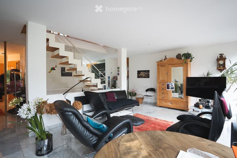 A modern living room with a black leather sofa, matching chairs, a wooden coffee table, a large wooden cabinet with a mirror, a television, and decorative plants.