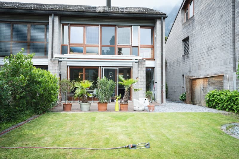 Well-maintained garden with a lawn, potted plants, and a modern house in the background.