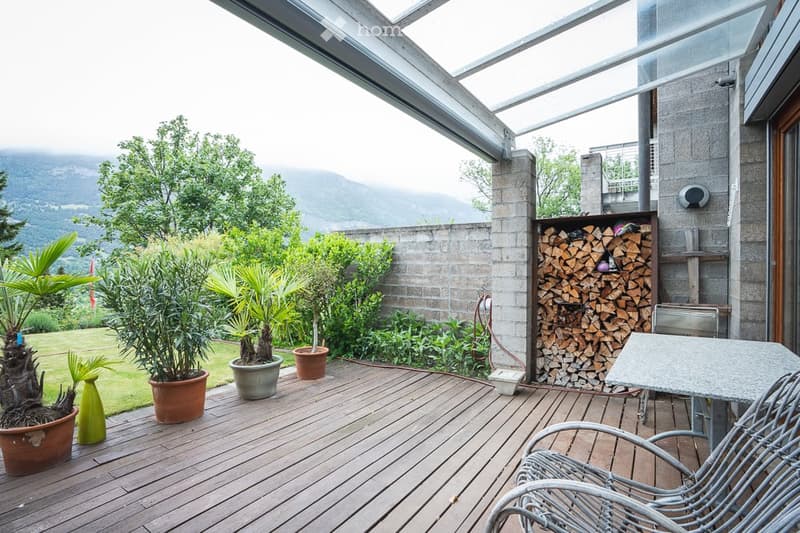 Wooden deck with potted plants, a stack of firewood, and outdoor furniture, overlooking a scenic mountain view.