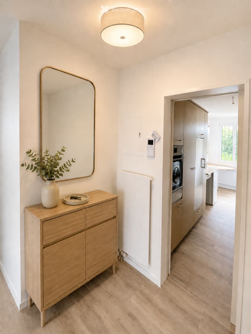 A modern hallway with light wooden flooring, a built-in wardrobe, a wooden console table with a vase and keys, and a large mirror on the wall.