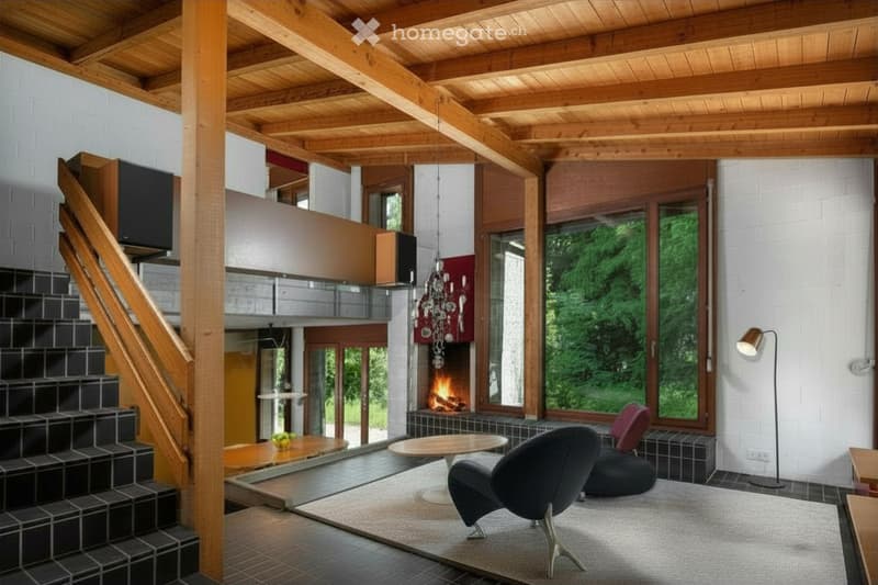Modern living room with exposed wooden beams, large windows offering a view of greenery, a fireplace, a sofa, a table, and a floor lamp.