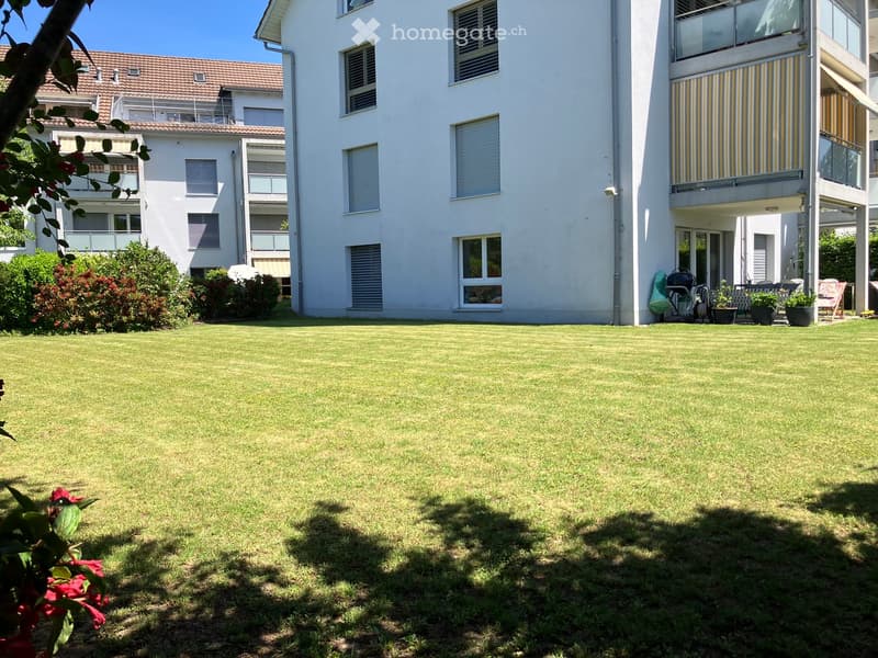 Well-maintained lawn in front of a multi-story residential building with balconies and windows, surrounded by greenery and shrubs.