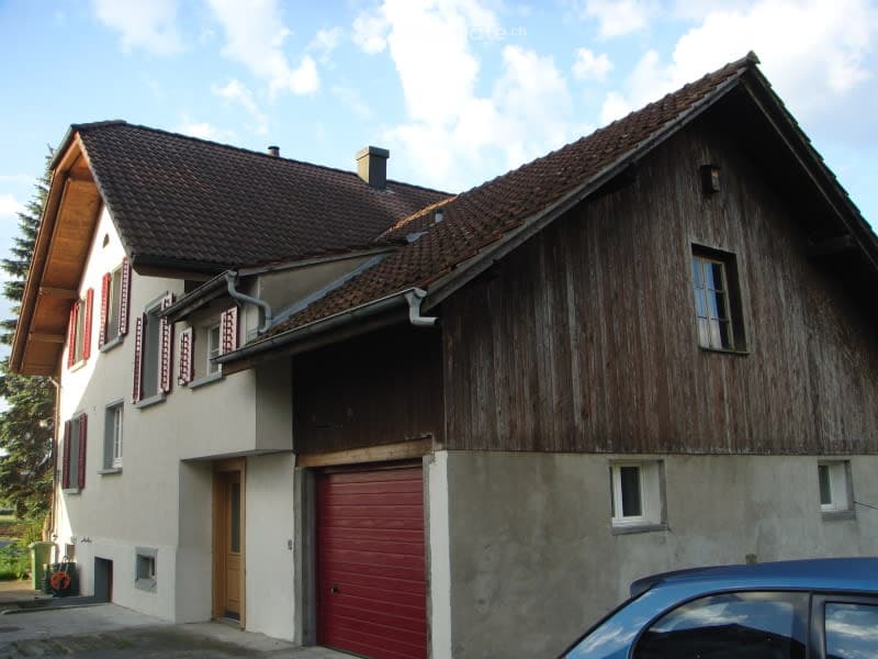 Two-story house with a red garage door, wooden siding, and red shutters on the windows.