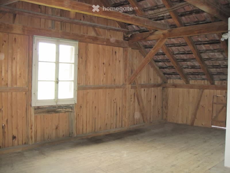 Empty wooden room with exposed beams and a single window, featuring wooden walls and floor.