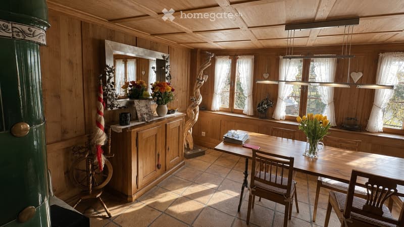 Cozy wooden-paneled room with a dining table, chairs, cabinet, mirror, and decorative items including vases with flowers.